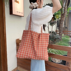 Detail view of the orange and white checkered canvas tote bag worn by a model in a garden