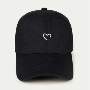 Detail of a black cotton baseball cap featuring a small white embroidered heart on the front