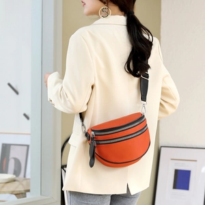 Orange half-moon crossbody bag with wide black strap worn by a model in a beige suit