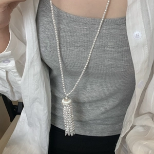 Detailed close-up of a long pearl necklace with tassel pendant on a model