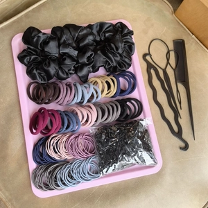 Flat lay of satin scrunchies, colorful hair ties, and black styling tools in a pink tray