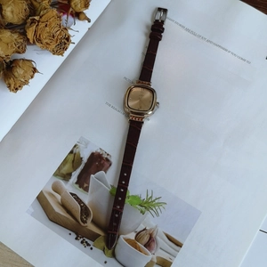 Detail of square gold quartz watch with brown leather strap on vintage book background