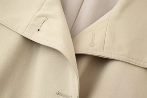 Detail of high-density twill cotton fabric and precise stitching on beige trench coat