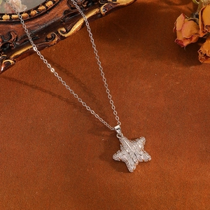 Detailed view of a silver star pendant with tiny clear crystals on brown velvet background