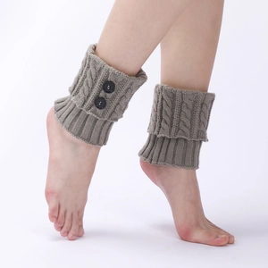 Detailed knit texture of beige leg warmers featuring cable patterns and black buttons