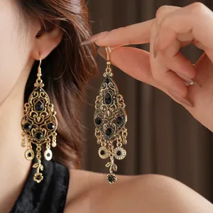 Vintage hollow gold drop earrings with black rhinestones and flower charms on model