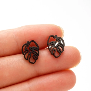 Macro shot of black hollow monstera leaf stud earrings on finger showing size and detail
