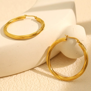 Gold twisted hoop earrings in titanium steel displayed on a beige stone platform
