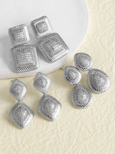 Detalle de pendientes geométricos plateados con pavé de circonitas y textura de malla