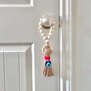 Detail of wooden bead door hanger with blue evil eye charm and jute tassel
