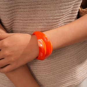 Detailed view of wide acrylic bangle with orange marble swirl on a model's wrist