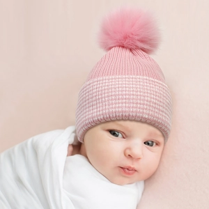Pink knit baby beanie with large faux fur pom and striped cuff for winter warmth