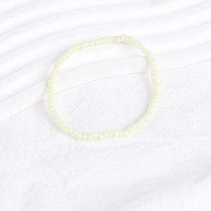 Close-up of minimalist cream yellow seed bead bracelet on a textured white surface