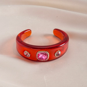 Close-up of orange resin cuff bracelet with pink crystals on champagne silk fabric