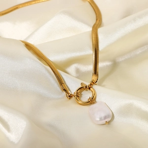 Macro shot of 18K gold plated snake chain with baroque pearl pendant on silk fabric