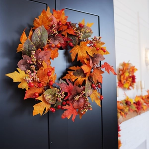 Autumn wreath with faux pumpkins and maple leaves hanging on dark door for fall decoration