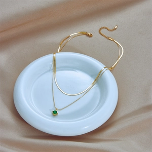 Double-layer gold necklace with emerald square pendant on a ceramic dish
