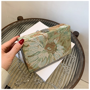 Detailed view of green and beige floral jacquard fabric and silver metal chain on handbag