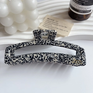 Detailed close-up of a square acetate hair claw clip with black and white spotted texture