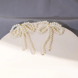 Detail of long pearl tassel bow earrings with golden metal links on a pedestal