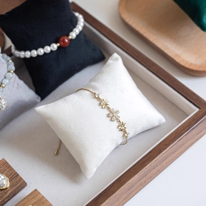 Velvet display pillow with elegant gold flower bracelets and pearl beads in a wooden tray