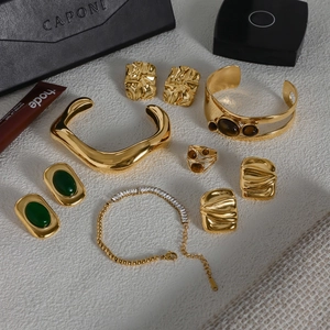 Detailed close-up of golden jewelry set with emerald and amber stones on textured surface