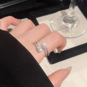Detail of elegant zircon and pearl open ring featuring a ribbon design on a model's finger