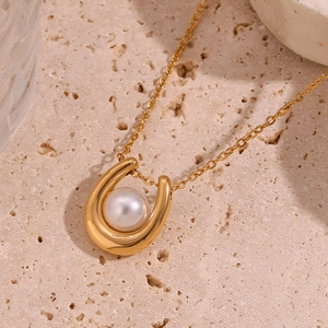 Macro detail of 18K gold-plated horseshoe pendant with white pearl on fine chain link