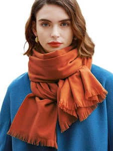 Close-up of vibrant orange cashmere-feel scarf with soft fringe detail on a model