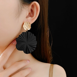 Close-up of golden hammered metal studs and large black textured floral pendant earrings