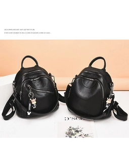 Detail view of two black soft leather backpacks featuring litchi grain and cute cow charm