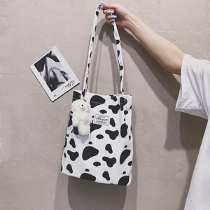 Detail of cow print canvas tote bag with a plush bear charm and stitched woven label