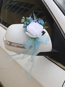 Close-up of a white silk rose wedding car mirror decor with blue berries and gold-edged ribbons