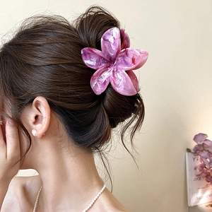 Detail shot of a purple plumeria hair claw clip used in a stylish updo for women