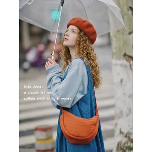 Bright orange nylon crescent crossbody bag in a stylish outdoor urban street setting