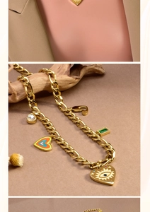 Detail of gold Cuban chain necklace with heart charms, sun eye pendant and green gemstone