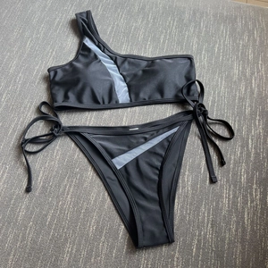 Detail of one-shoulder black bikini with sheer mesh panel and side tie bottoms