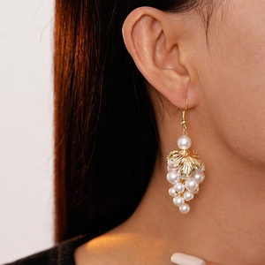 Detail of baroque pearl grape cluster earrings with golden leaf design on a model