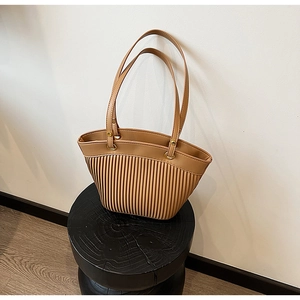 Close-up of khaki straw bag with vertical pleats and dual slim handles on a wooden stand