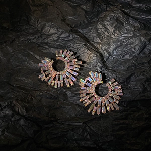 Macro shot of silver needle C-shaped radial earrings with iridescent crystals on black background