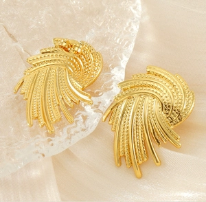 Detail view of gold irregular swirl earrings with granular texture on luxury silk fabric