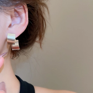 Close-up of minimalist square silver stud earrings featuring layered geometric metal design