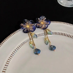 Close-up of blue floral tassel earrings with crystal drops on a ceramic plate