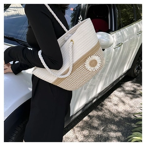 Detail of woven straw tote bag featuring a large white daisy flower and rope handles