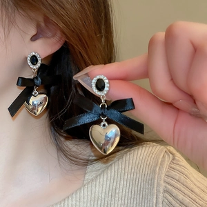 Detail of silver needle earrings featuring black flocking, silk bow, and heart metal charms