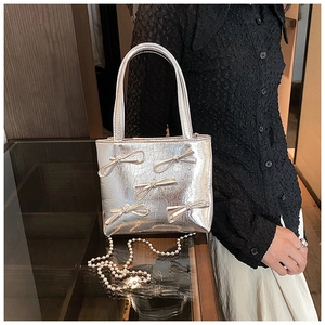 Detail of silver handbag featuring 3D bows and a pearl chain strap on smooth leather
