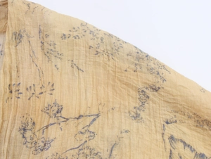 Macro detail of breathable pleated fabric with blue floral print on light yellow background