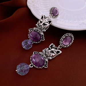 Detail view of vintage cat earrings with purple gemstones on elegant dark fabric