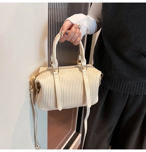 Detailansicht einer cremefarbenen Handtasche mit eleganter Faltenstruktur und Goldbeschlägen