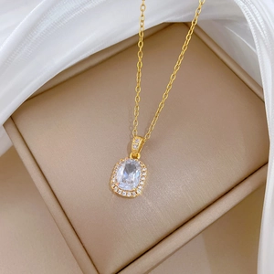 Close-up of gold titanium necklace with zircon square pendant on beige jewelry box